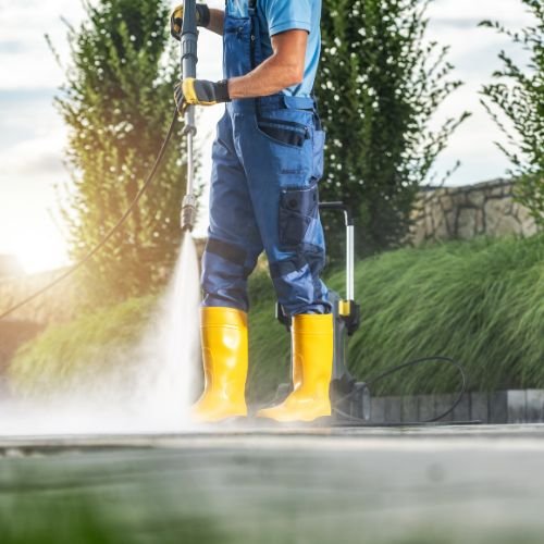 A worker in protective gear operating a pressure washer.