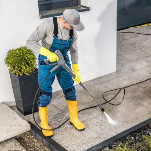 A person in overalls and rubber boots washing a patio surface. Pressure Washing Company Florida